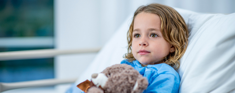 Kind im Krankenhausbett mit Teddybär