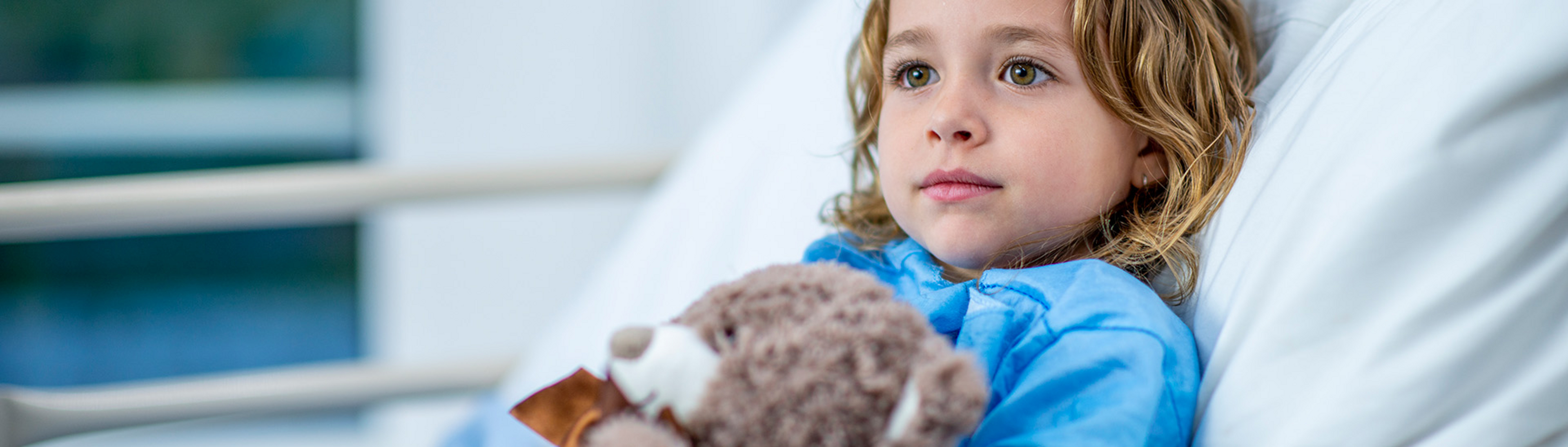 Kind im Krankenhausbett mit Teddybär