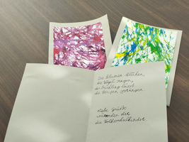Drei открытки mit bunten Bildern und handschriftlichem Gedicht stehen auf einem Tisch.