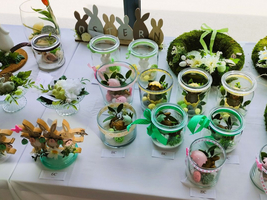 Bunte Osternester in Gläsern, dekoriert mit Blumen und kleinen Möhrenfiguren.