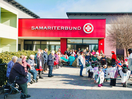 Ältere Menschen und Kinder feiern vor dem Samaritersbund-Gebäude.