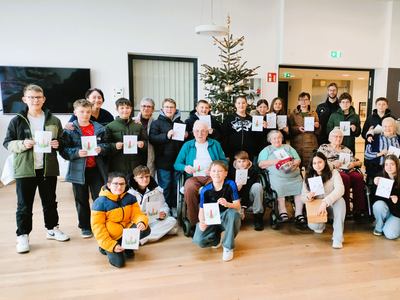 Eine Gruppe von Menschen hält Karten vor einem Weihnachtsbaum in einem Gemeinschaftsraum.