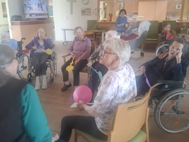 Ältere Menschen sitzen in einem Raum und interagieren miteinander, einige halten Ballons.