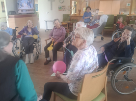 Ältere Menschen sitzen in einem Raum und interagieren miteinander, einige halten Ballons.