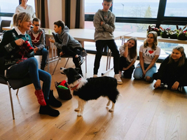 Eine Frau sitzt mit einem Hund, umgeben von aufmerksam zuschauenden Kindern.