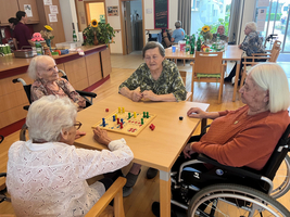 Vier ältere Frauen spielen zusammen ein Brettspiel in einem Gemeinschaftsraum.