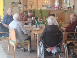 Eine Gruppe älterer Menschen sitzt zusammen und genießt Musik von einem Akkordeonspieler.