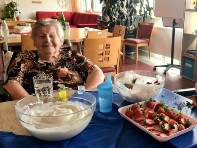 Zwei ältere Frauen bereiten zusammen Erdbeeren und Sahne in einer Küche vor.