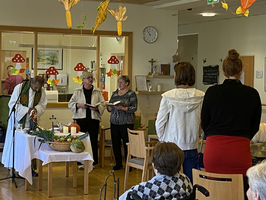 Ein Gottesdienst mit zwei Frauen und einem Geistlichen in einem Gemeinschaftsraum.