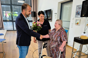 Ein Mann überreicht einer älteren Frau einen Blumenstrauß und schüttelt ihre Hand.