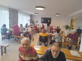 Eine Gruppe älterer Menschen in einem Gemeinschaftsraum mit Tischen und Stühlen.