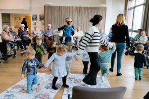 Kinder tanzen und spielen mit Betreuern in einem Raum mit älteren Menschen.
