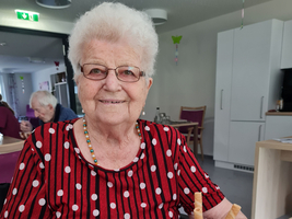 Eine ältere Frau mit Brille lächelt und hält ein Eisbecher in der Hand.