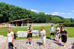Gruppe von Menschen in der Natur, vor einem Pferdestall auf grüner Wiese.