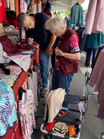 Eine ältere Frau betrachtet Kleidung mit Hilfe eines Mannes auf einem Markt.