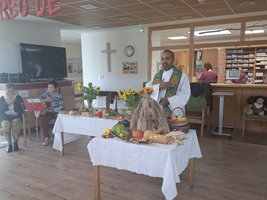 Ein Mann im Priestergewand steht an einem Tisch mit Herbstdekoration.