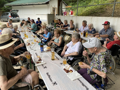 Ältere Menschen genießen ein gemeinsames Essen an einem langen Tisch im Freien.