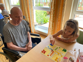 Ein älterer Mann und ein Mädchen spielen ein Brettspiel am Tisch.