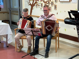 Zwei Männer spielen zusammen auf Akkordeons in einem gemütlichen Raum.