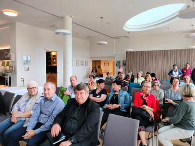 Eine Gruppe von Menschen sitzt in einem modernen Raum und hört aufmerksam zu.