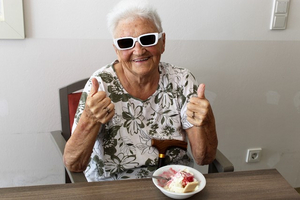 Ältere Frau mit Sonnenbrille gibt Daumen nach oben neben einer Eisschüssel.