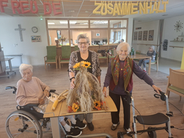 Drei ältere Frauen stehen an einem Tisch mit einer Dekoration aus Sonnenblumen.