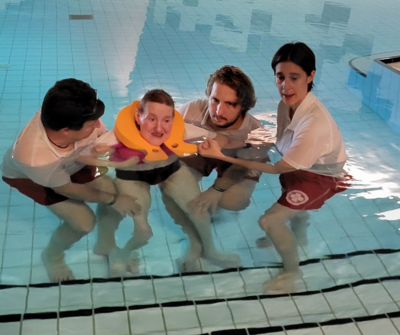 Vier Personen helfen einem Mann mit einem Schwimmring im Wasser.