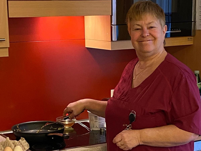 Eine lächelnde Frau kocht in einer modernen Küche mit roten Wänden.