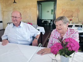 Ein älteres Paar sitzt an einem Tisch mit einer blühenden Pflanze.