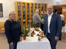 Zwei Personen stehen vor einem Tisch mit weihnachtlicher Dekoration in einem Raum.