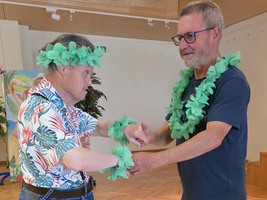 Zwei Männer tragen Blumenkränze und tanzen in einem Raum.