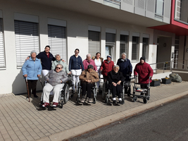 Gruppe älterer Menschen in Rollstühlen mit Pflegepersonal vor einem Gebäude.