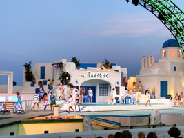 Bühne mit Darstellern vor einem griechischen Taverna-Hintergrund bei Sonnenuntergang.