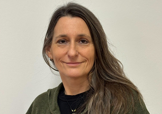 Eine Frau mit langen, braunen Haaren lächelt freundlich in die Kamera.