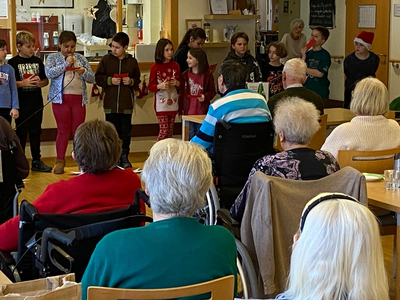 Kinder führen ein Weihnachtsprogramm für Senioren in einem Gemeinschaftsraum auf.