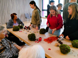 Ältere und jüngere Menschen basteln zusammen mit Naturmaterialien an einem Tisch.