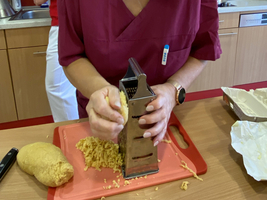 Eine Person reibt Käse mit einer Reibe in einer Küche.