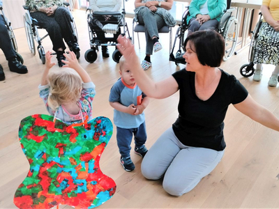 Eine Pädagogin tanzt mit Kindern in einem Raum voller älterer Menschen.