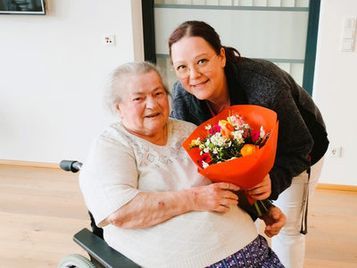 Eine Frau überreicht einer älteren Dame einen Blumenstrauß.