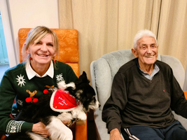 Eine Frau mit Hund sitzt neben einem lächelnden älteren Mann.