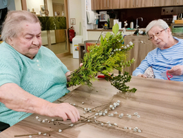 Mehrere ältere Frauen in Rollstühlen halten Blumenarrangements und lächeln.