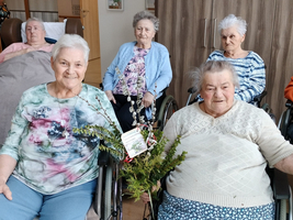Mehrere ältere Frauen in Rollstühlen halten Blumenarrangements und lächeln.