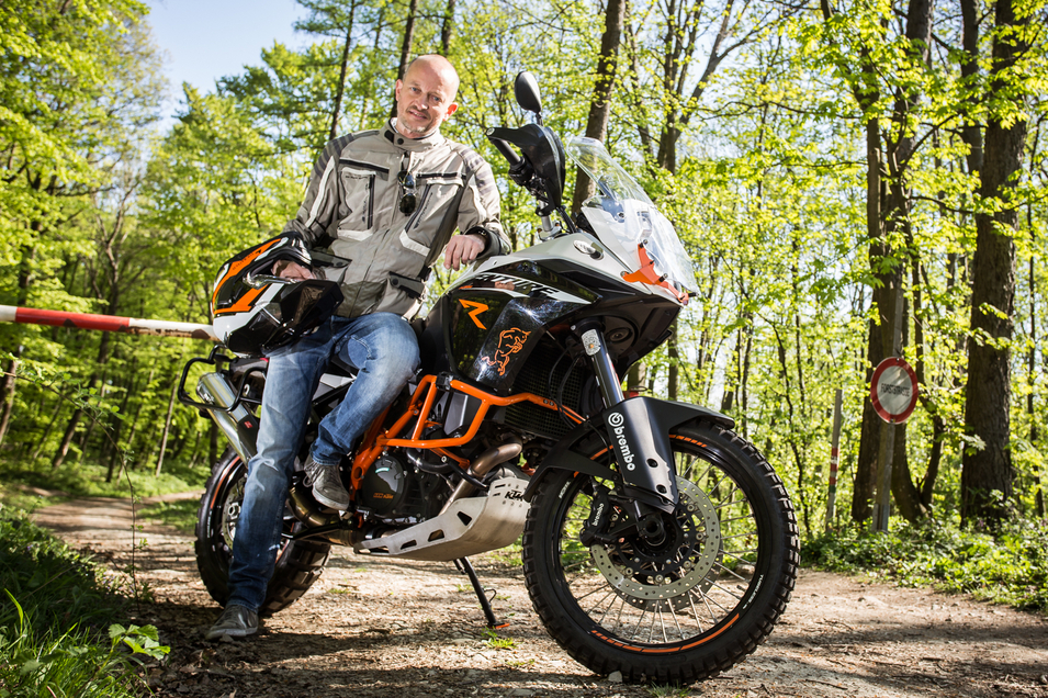 Motorradfahrer lehnt seitlich an Motorrad und befindet sich im Wald
