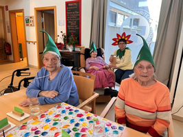 Gruppierung älterer Menschen mit Hüten, die an einer Aktivität in einem Gemeinschaftsraum teilnehmen.