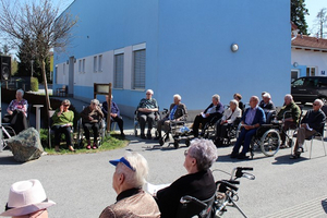 Ältere Menschen sitzen im Freien und hören einer Veranstaltung zu.