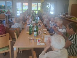 Eine Gruppe älterer Menschen sitzt an einem Tisch und applaudiert.