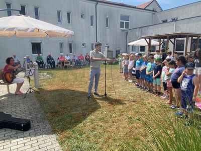 Kinder stehen in einer Reihe, während eine Musikerin mit Gitarre spielt.