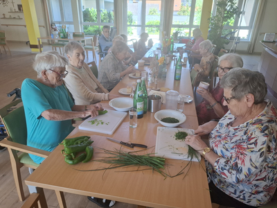 Ältere Frauen bereiten gemeinsam frische Lebensmittel an einem Tisch vor.