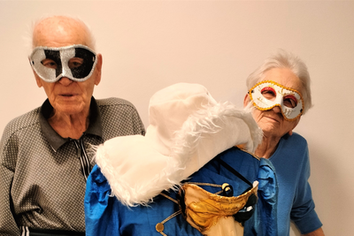 Zwei ältere Menschen mit Masken stehen neben einem kostümierten Dummy.