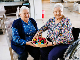 Zwei ältere Damen halten einen Korb mit bunten Eiern in der Hand.